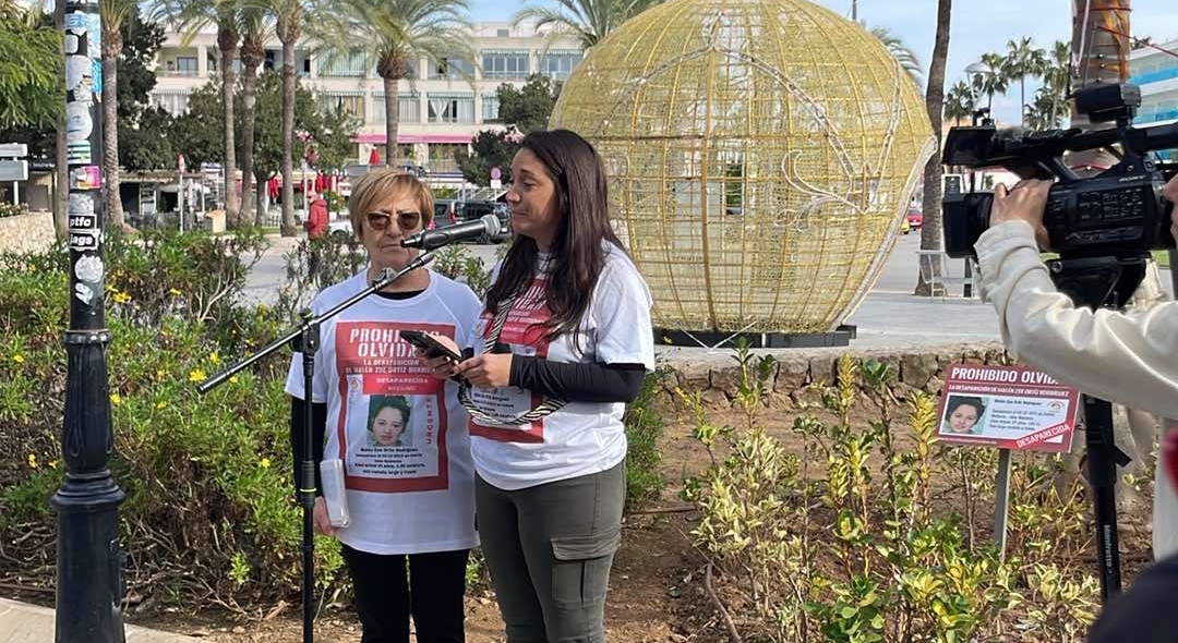 Dos mujeres hablando en un evento con carteles de Malen Ortiz.