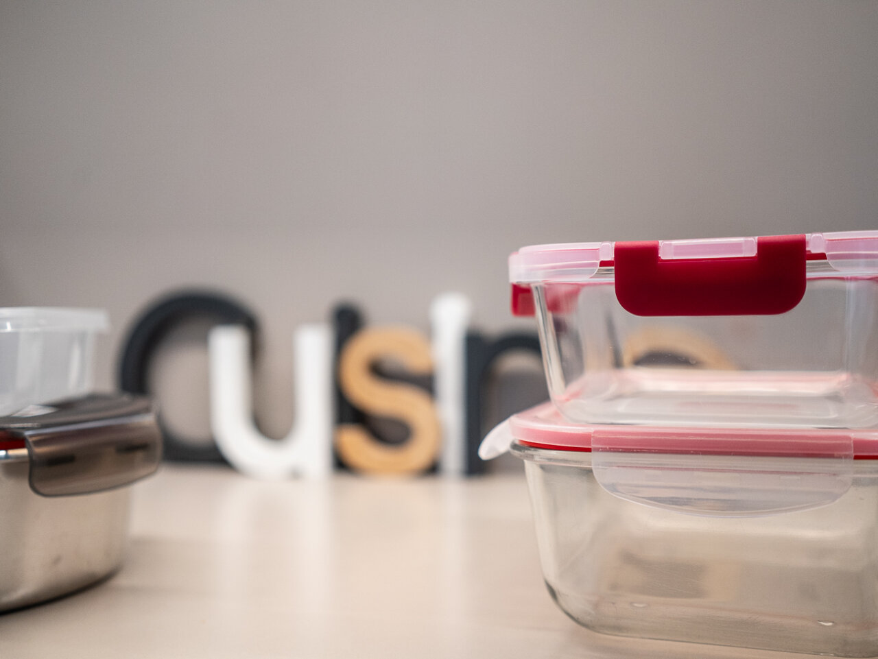Tuppers de vidrio apilados sobre una mesa con letras decorativas.