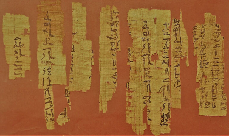 Fragmentos de papiro antiguo con escritura jeroglífica en fondo rojo.