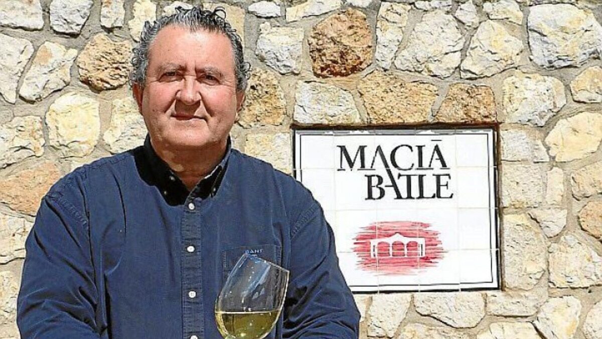 Ramon Servalls sosteniendo una copa de vino frente a un cartel de Macia Batle.