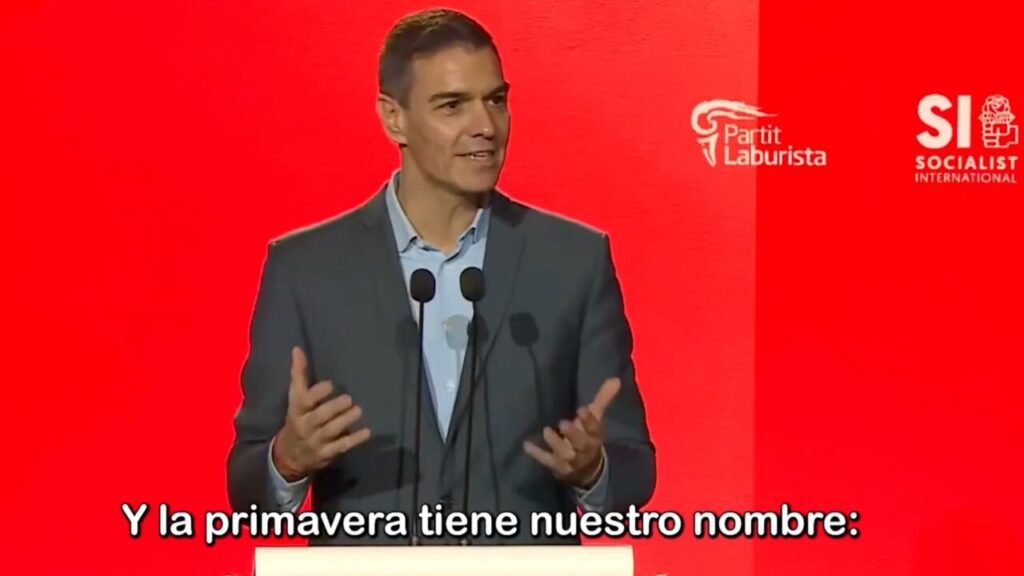 Pedro Sánchez hablando en un evento político con fondo rojo