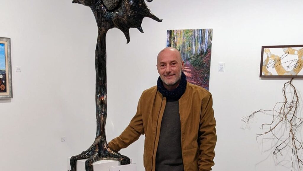 Toni Coll posando junto a una escultura en una galería de arte