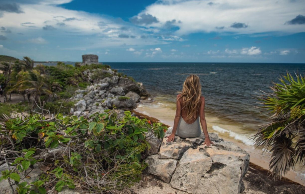 Mujer sentada en una roca mirando el mar en Tulum