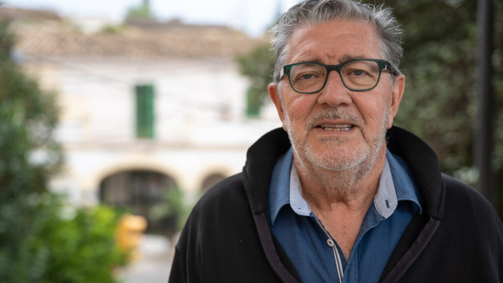 Hombre mayor sonriendo en un entorno urbano con edificios de fondo