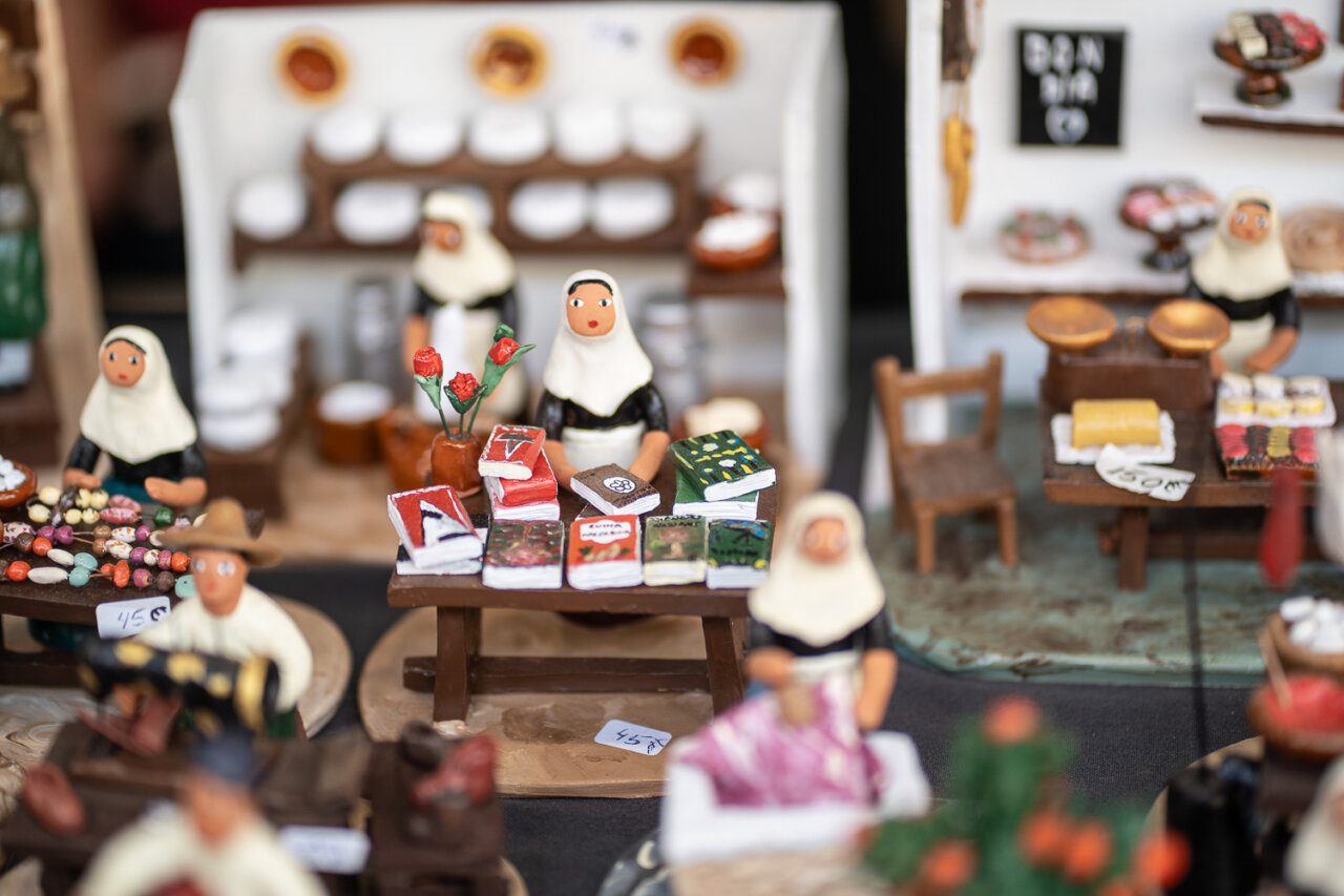 Figuras de artesanos en un mercado navide&ntilde;o con productos t&iacute;picos.