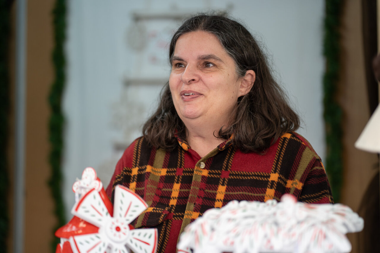 Mujer sonriente mostrando artesanías navideñas en un mercado.