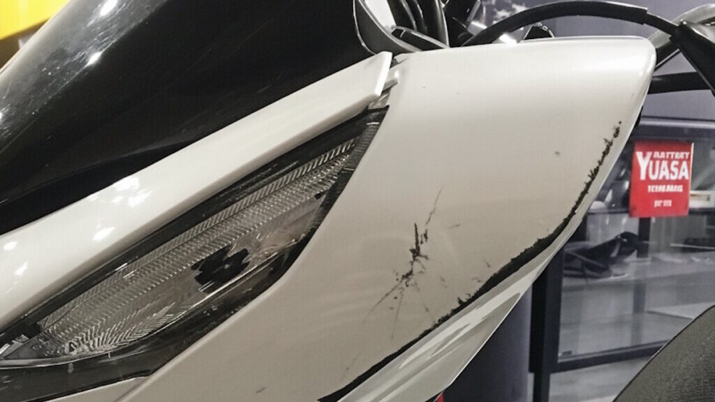 Motocicleta blanca con da&ntilde;os visibles en el lateral