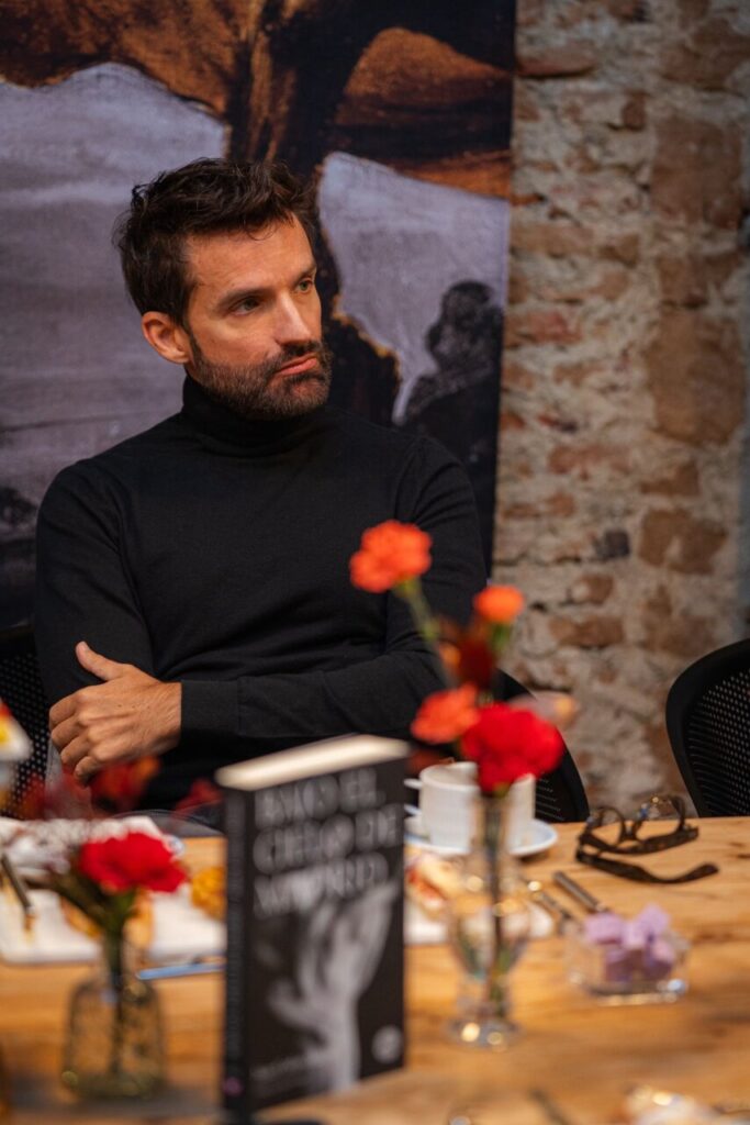 Hombre pensativo en una mesa con flores y un libro.