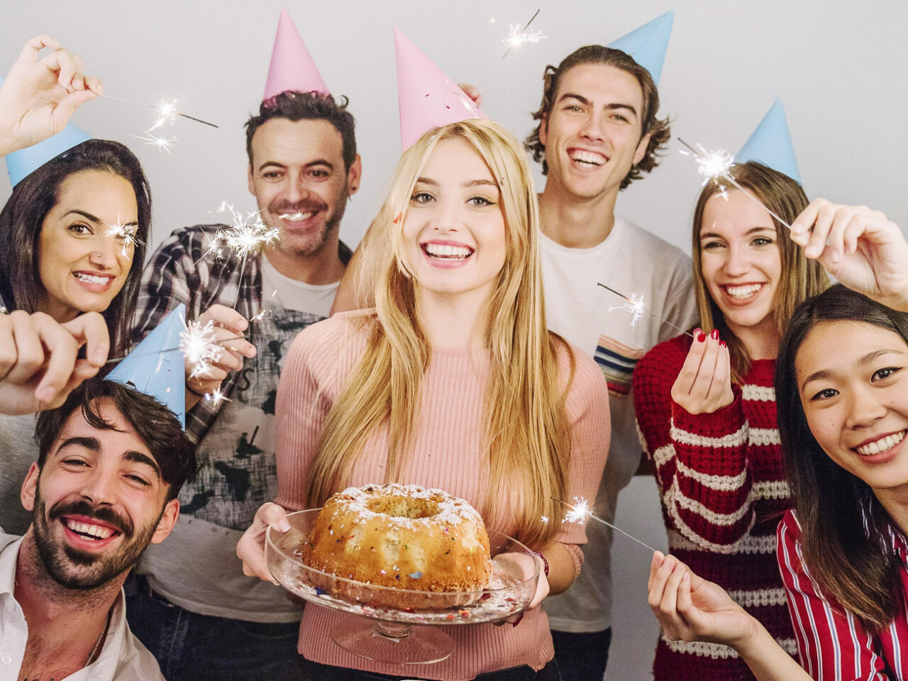Grupo de amigos celebrando con gorros de fiesta y fuegos artificiales