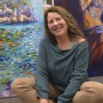 Dolors Mart&iacute; sonriendo en su estudio rodeada de pinturas coloridas.