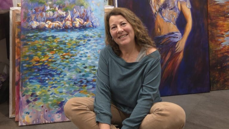 Dolors Martí sonriendo en su estudio rodeada de pinturas coloridas.