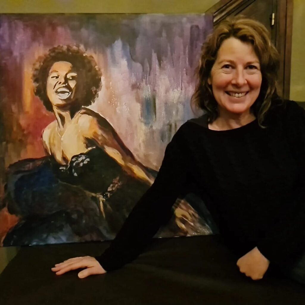 Dolors Mart&iacute; sonriendo junto a su pintura en un ambiente art&iacute;stico.