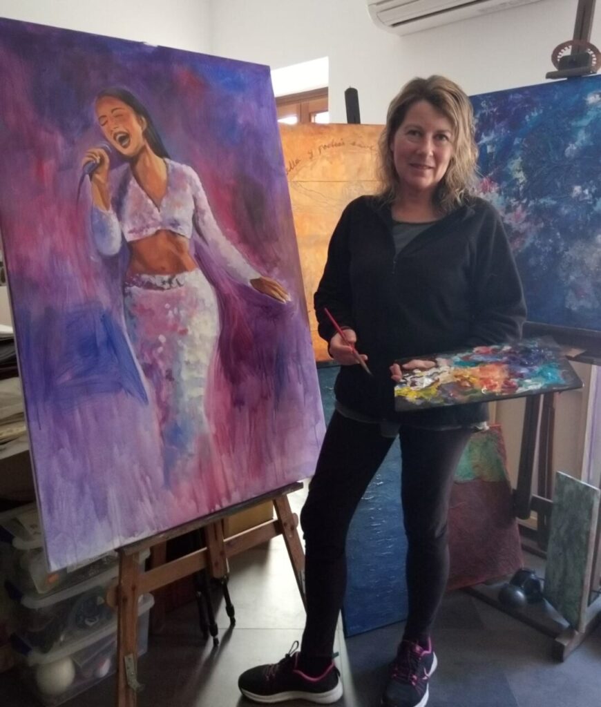 Artista Dolors Mart&iacute; pintando en su estudio con un cuadro de fondo