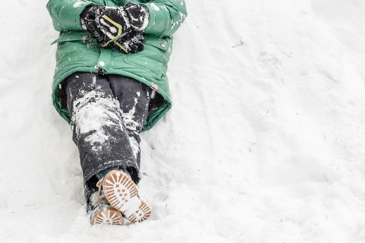 Persona sentada en la nieve con abrigo verde y guantes