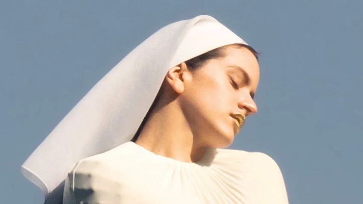 Rosalía con un vestido blanco y velo en un fondo azul