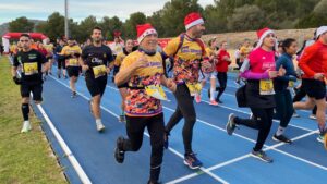 Participantes corriendo en la Hidrobal Sant Silvestre Calvianera con gorros navide&ntilde;os.