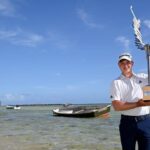 Jayden Schaper celebrando su victoria en el AfrAsia Bank Mauritius Open con un trofeo en la playa.