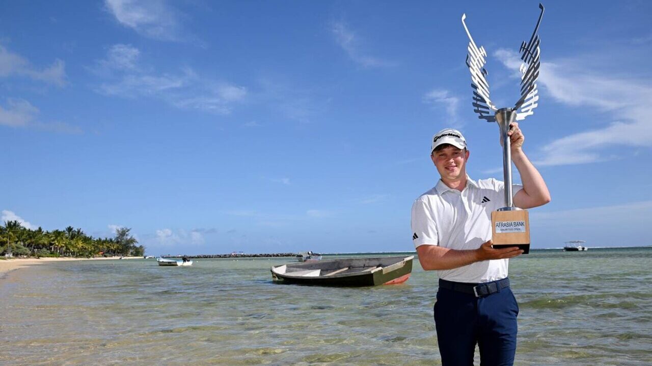 Jayden Schaper celebrando su victoria en el AfrAsia Bank Mauritius Open con un trofeo en la playa.