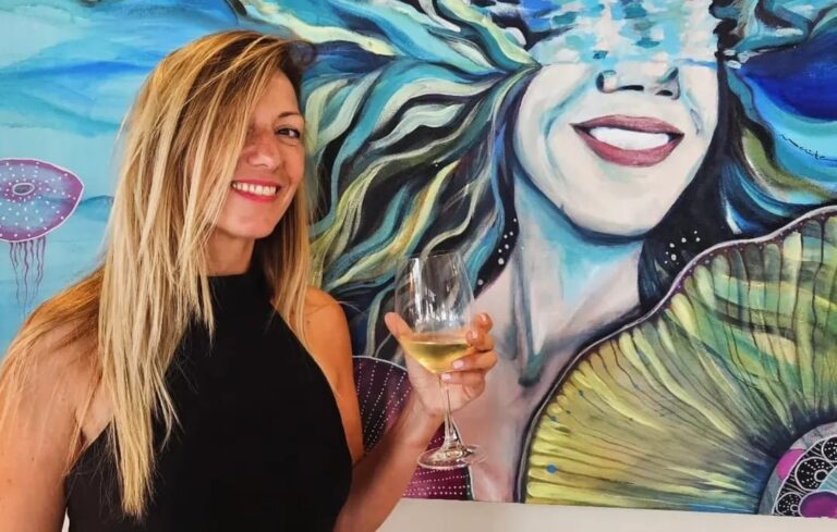 Maite Granados sosteniendo una copa de vino junto a su obra de arte