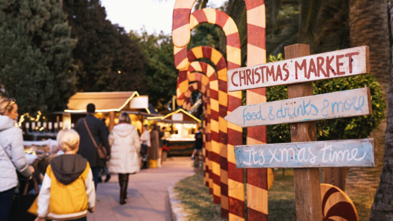 Visitantes en el mercado navideño de Puerto Portals con decoraciones festivas.