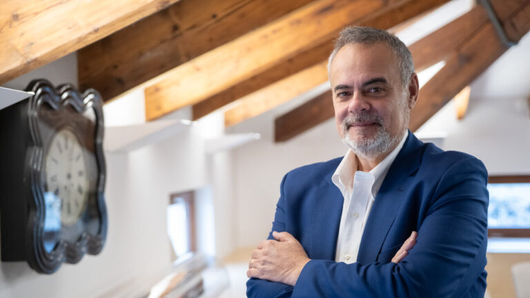 Hombre con barba y chaqueta azul sonriendo en un ambiente moderno.