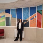 Silvina Barrera de pie junto a murales coloridos en una sala.