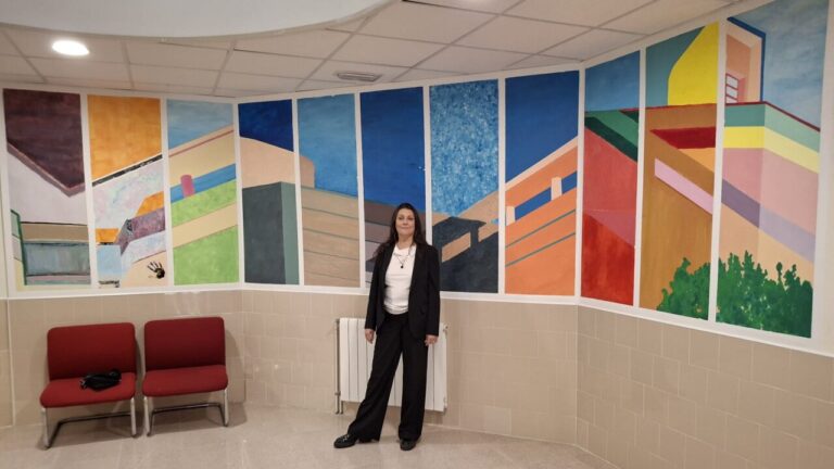 Silvina Barrera de pie junto a murales coloridos en una sala.