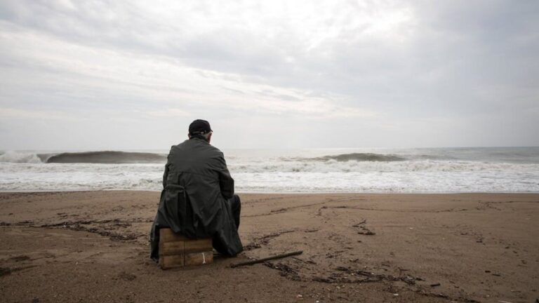 Hombre sentado en la playa mirando al mar en un d&iacute;a nublado