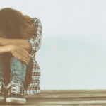 Persona con cabello largo abrazando sus piernas en un ambiente triste