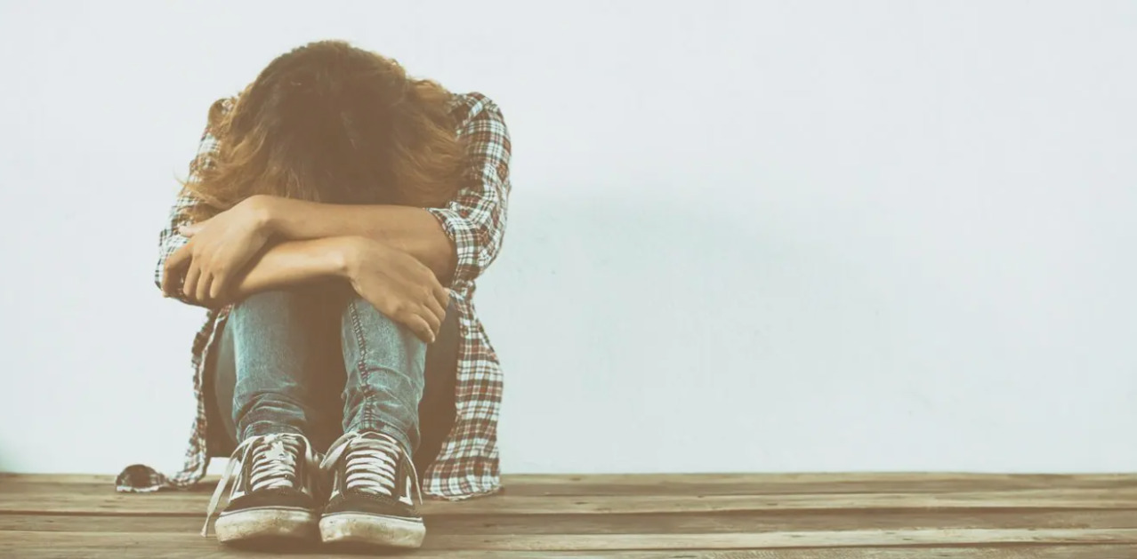 Persona con cabello largo abrazando sus piernas en un ambiente triste