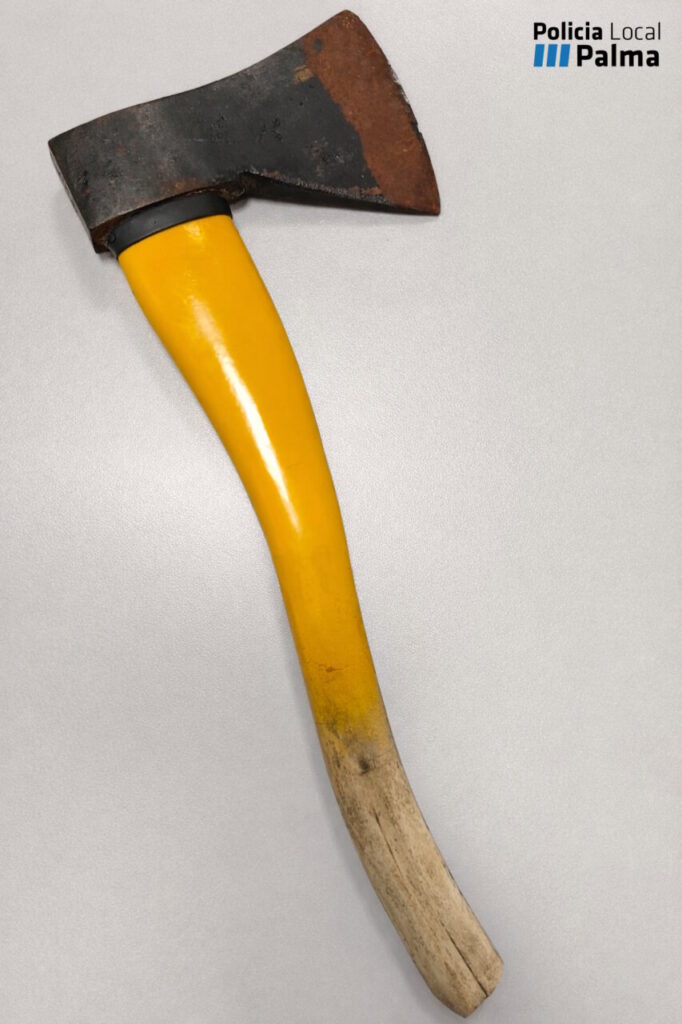 Hacha de mano con mango amarillo y hoja oxidada sobre fondo gris