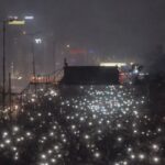 Multitud de personas en protesta con luces encendidas en la noche