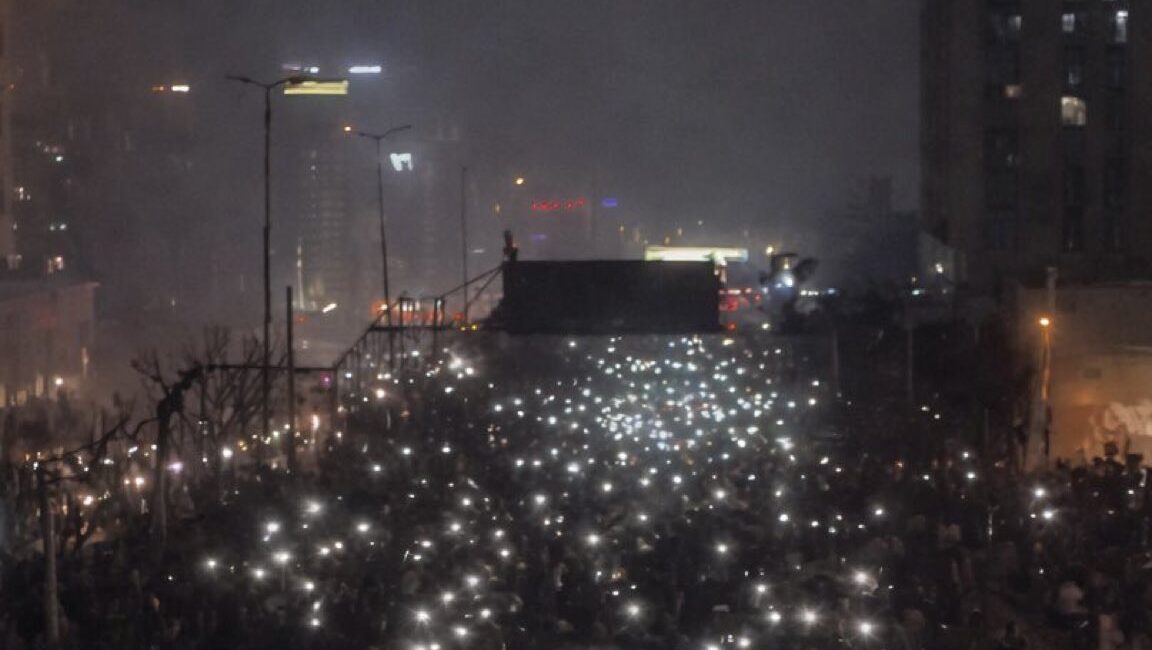 Multitud de personas en protesta con luces encendidas en la noche