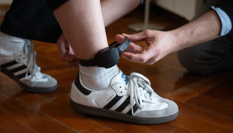 Persona colocando una pulsera electr&oacute;nica de geolocalizaci&oacute;n en el tobillo.