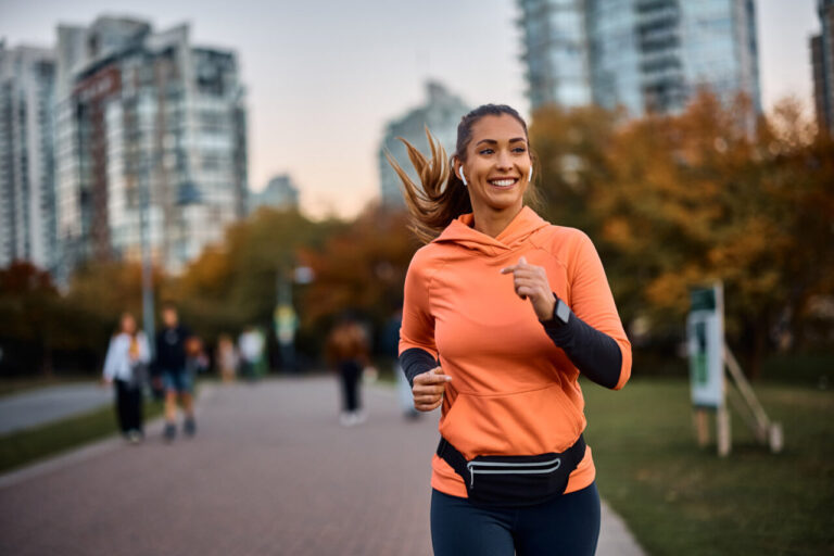 Mujer corriendo en un parque con ropa deportiva y sonrisa