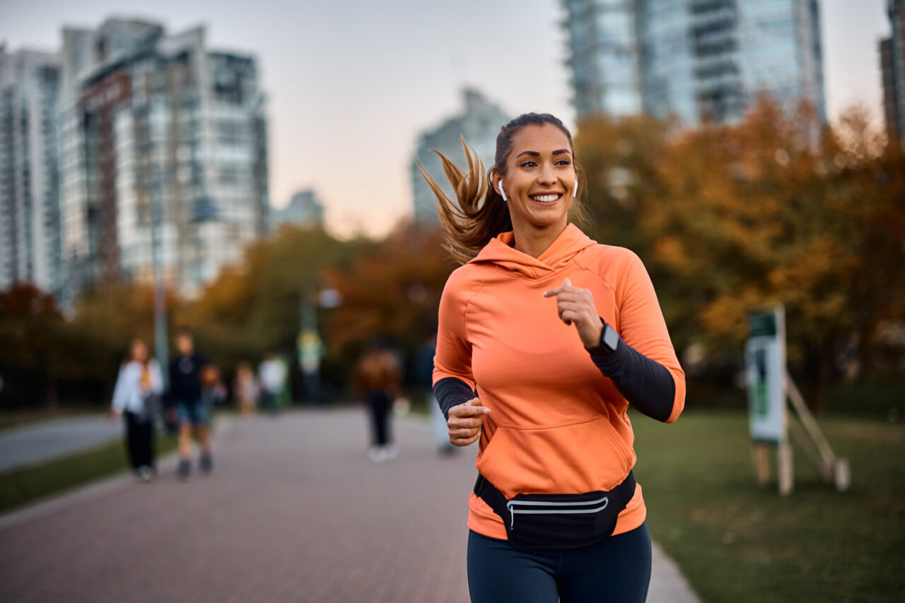 Mujer corriendo en un parque con ropa deportiva y sonrisa