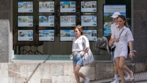 Mujeres caminando frente a una inmobiliaria con anuncios de vivienda