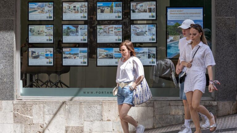 Mujeres caminando frente a una inmobiliaria con anuncios de vivienda