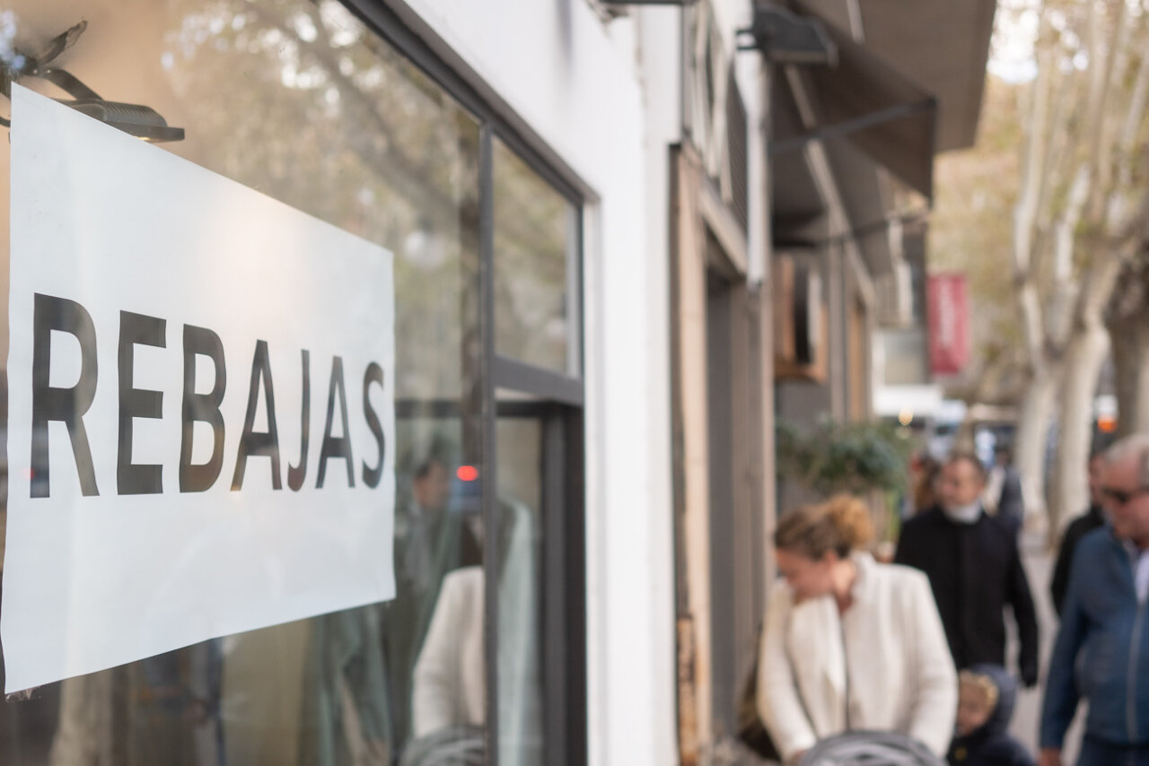 Cartel de rebajas en una tienda en Baleares con gente de fondo