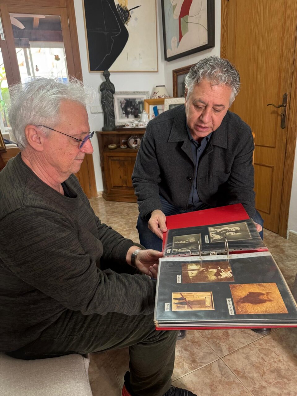 Dos hombres revisando un &aacute;lbum de fotos en una sala de estar