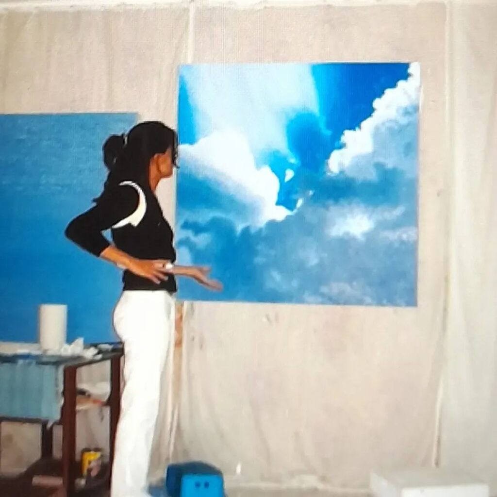 Silvina Barrera trabajando en una pintura con nubes y cielo azul.
