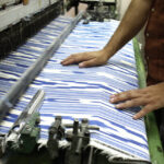 Manos trabajando en un telar con tela de rayas azules