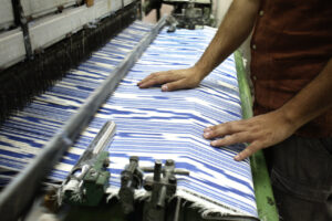 Manos trabajando en un telar con tela de rayas azules