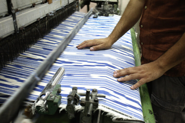 Manos trabajando en un telar con tela de rayas azules