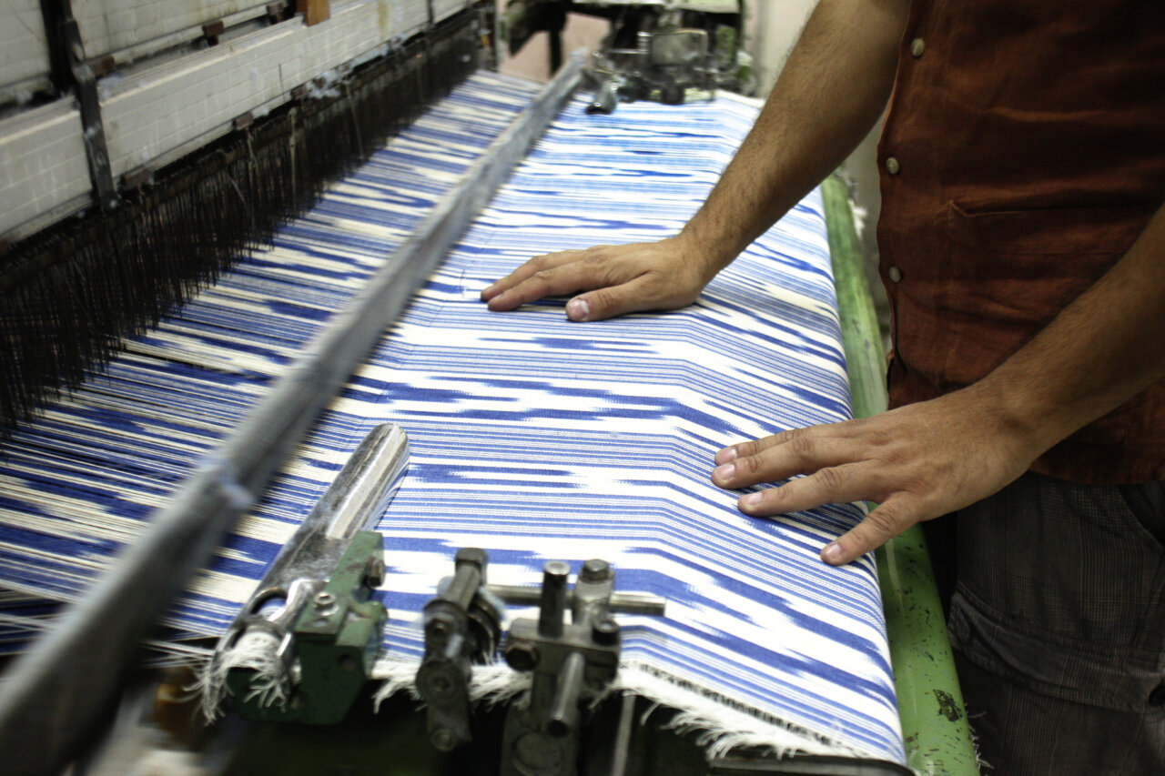 Manos trabajando en un telar con tela de rayas azules
