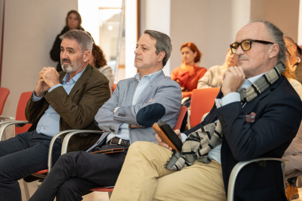 Tres hombres sentados en un evento, observando atentamente.