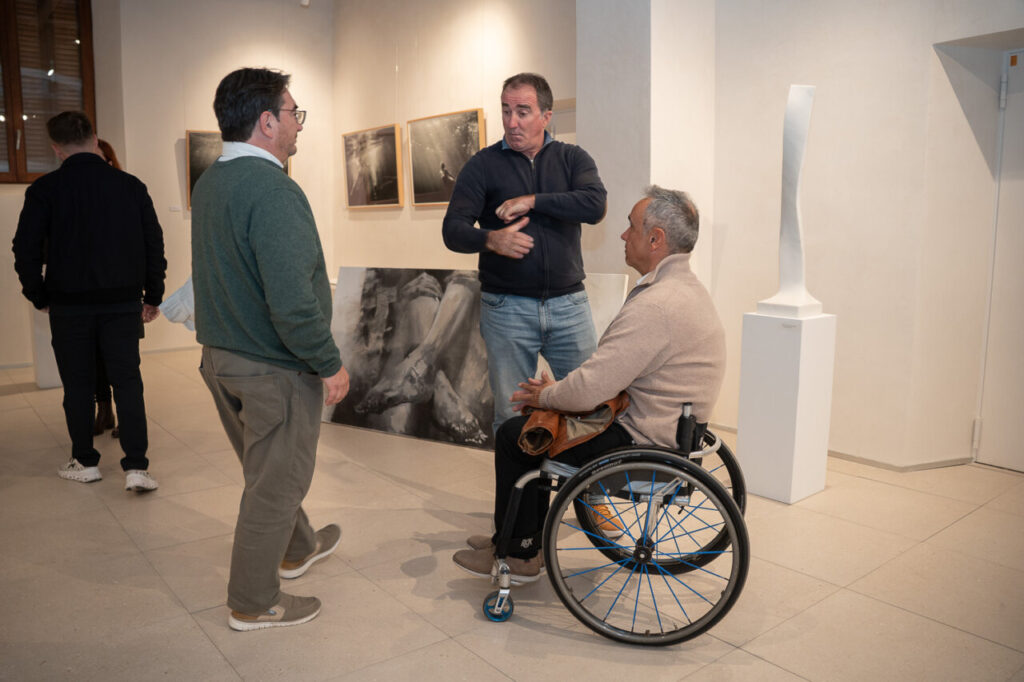 Tres hombres conversando en una galer&iacute;a de arte moderna.