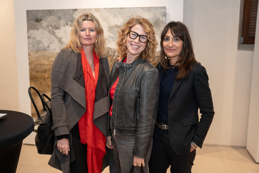 Tres mujeres posando en un evento con arte de fondo