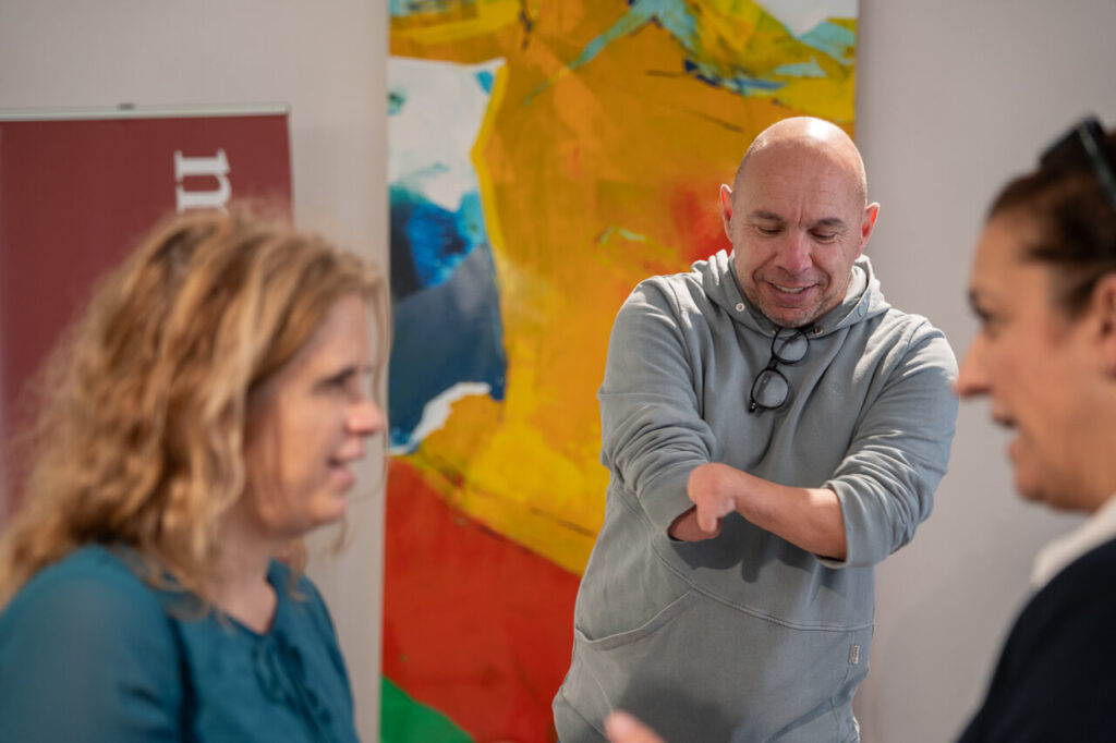 Personas interactuando en un evento con arte colorido de fondo