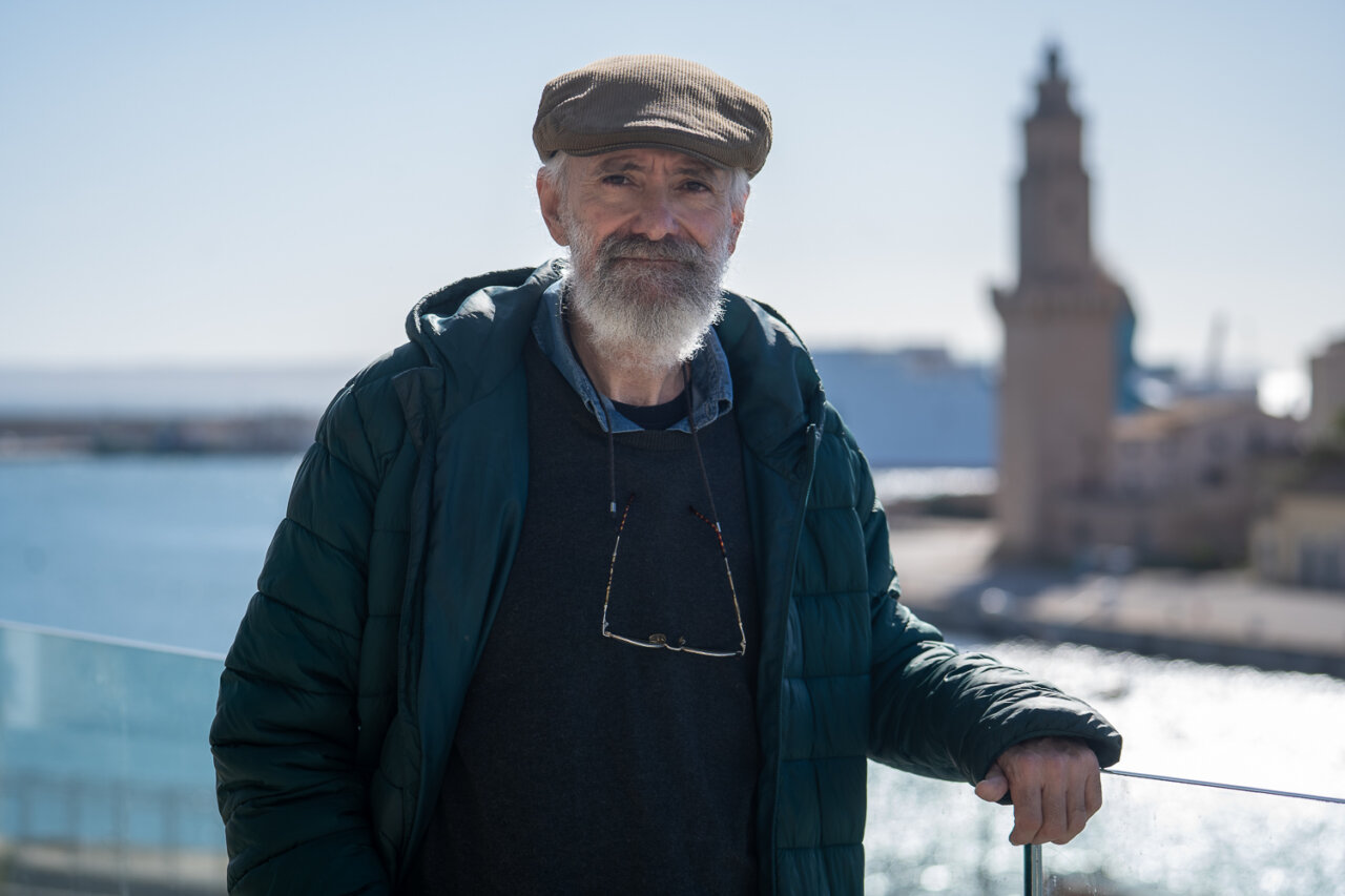 Hombre mayor con barba y gorra frente al Faro de Porto Pi